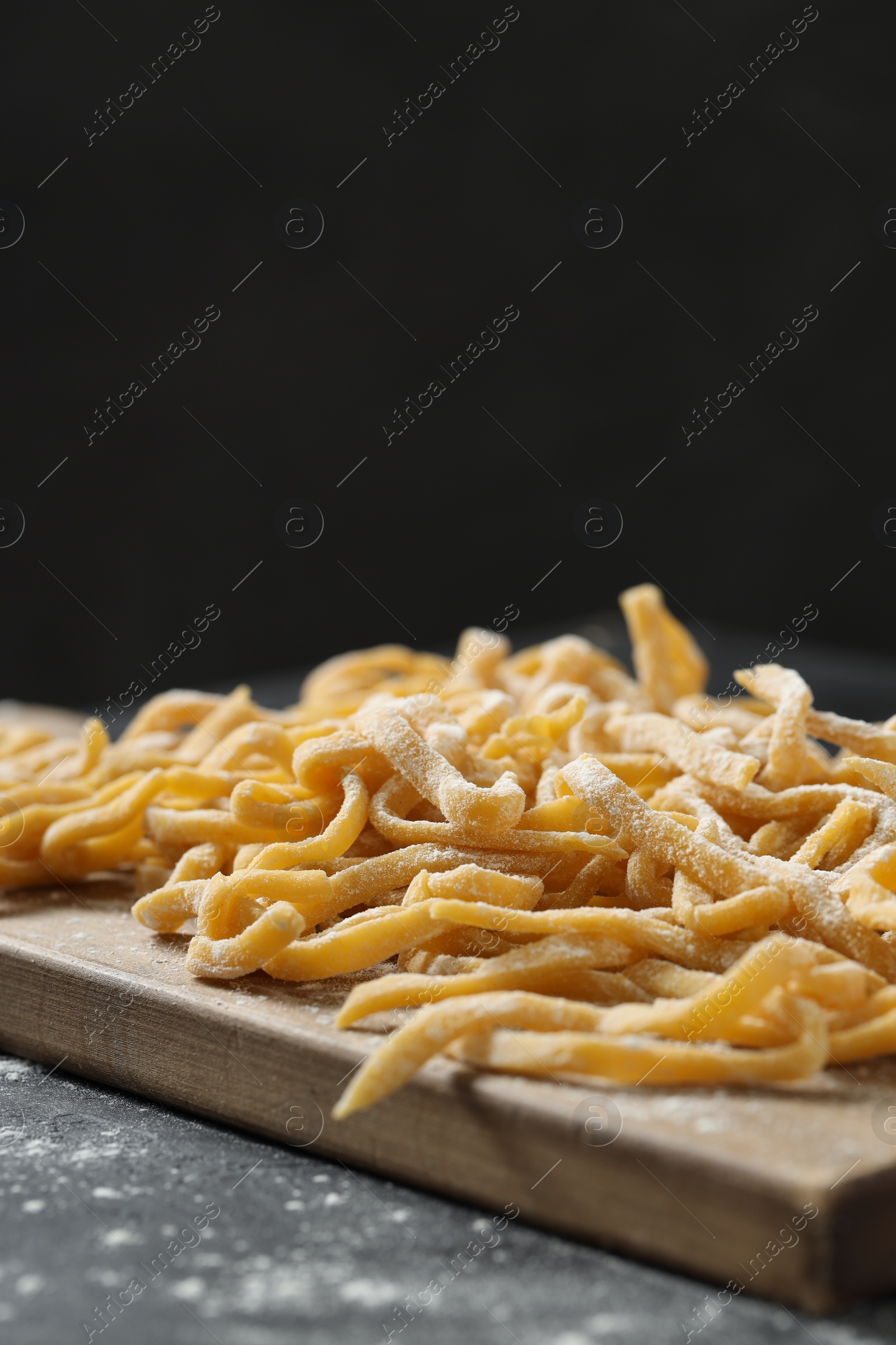 Photo of Board with homemade pasta and flour on dark table. Space for text