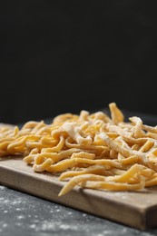 Photo of Board with homemade pasta and flour on dark table. Space for text