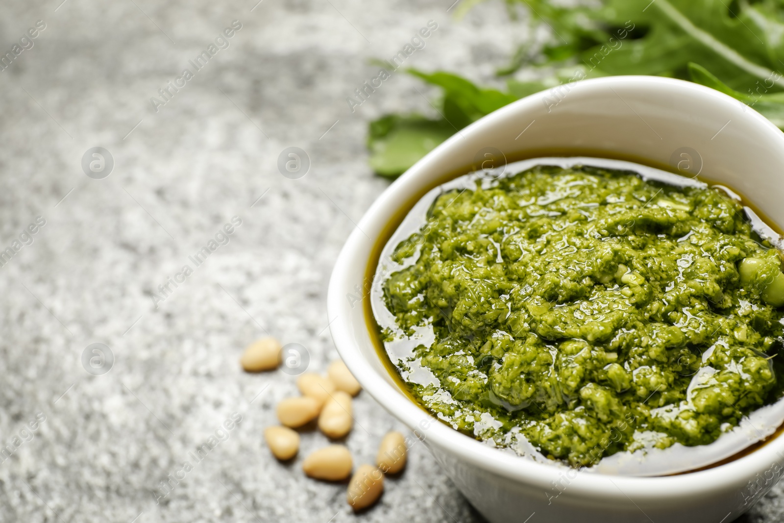 Photo of Bowl of tasty arugula pesto on grey table, closeup. Space for text