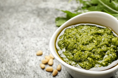 Bowl of tasty arugula pesto on grey table, closeup. Space for text