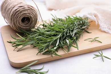 Photo of Fresh green rosemary twigs and twine on white wooden table, closeup