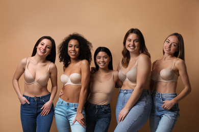 Group of women with different body types in jeans and underwear on beige background