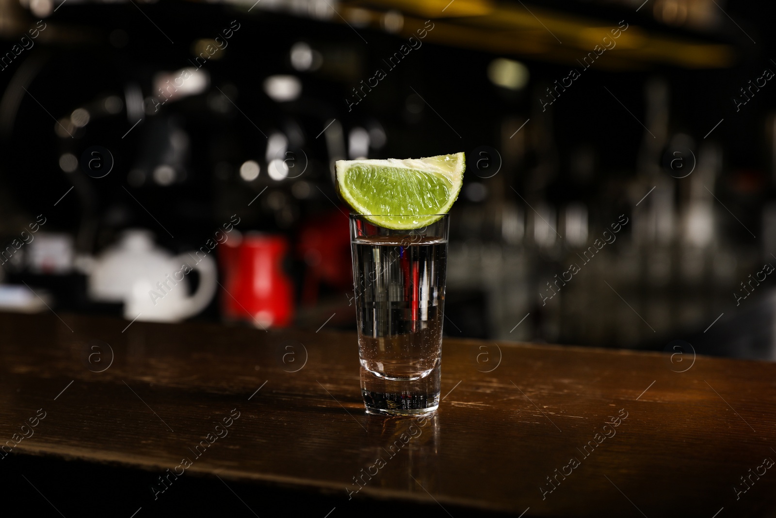 Photo of Mexican Tequila shot with lime slice on wooden bar counter