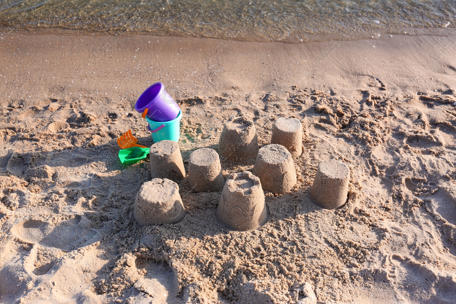 Photo of Little sand figures and plastic toys on beach near sea, above view