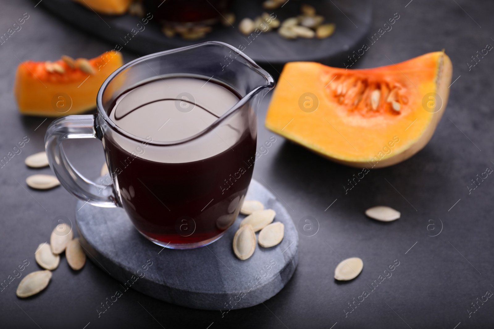 Photo of Fresh pumpkin seed oil in glass pitcher with seeds on dark grey table