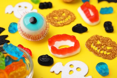 Tasty colorful jelly candies and Halloween decorations on yellow background, closeup