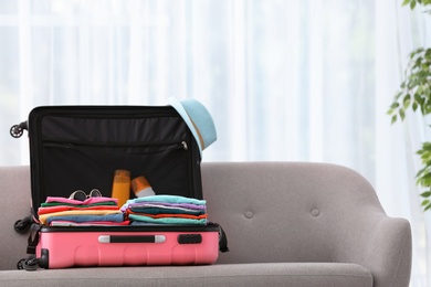 Photo of Modern suitcase full of clothes on sofa indoors. Space for text