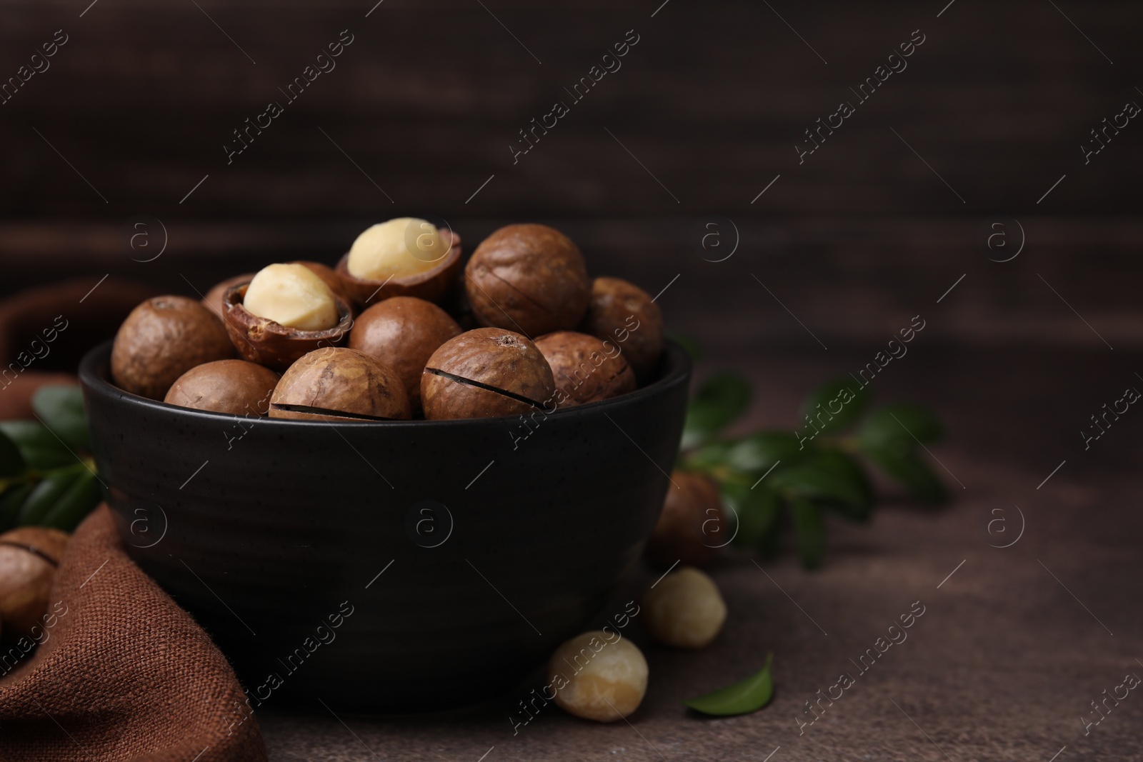 Photo of Tasty Macadamia nuts in bowl on brown table. Space for text