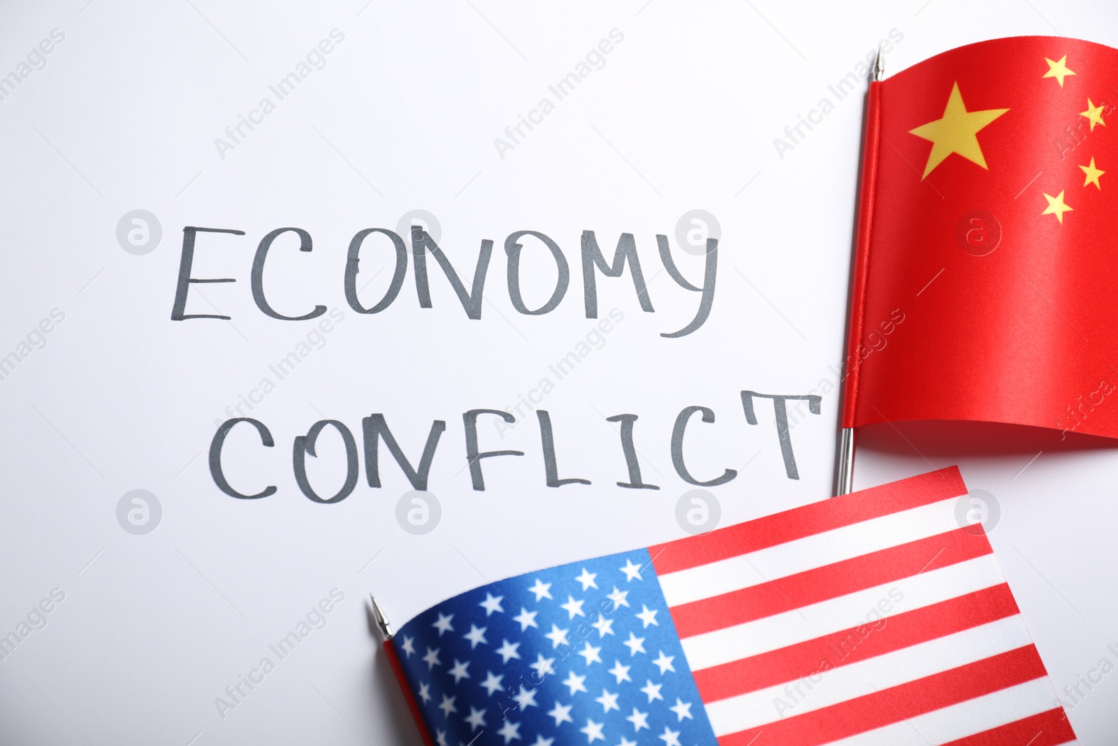 Photo of USA and China flags near words ECONOMY CONFLICT on white background, flat lay