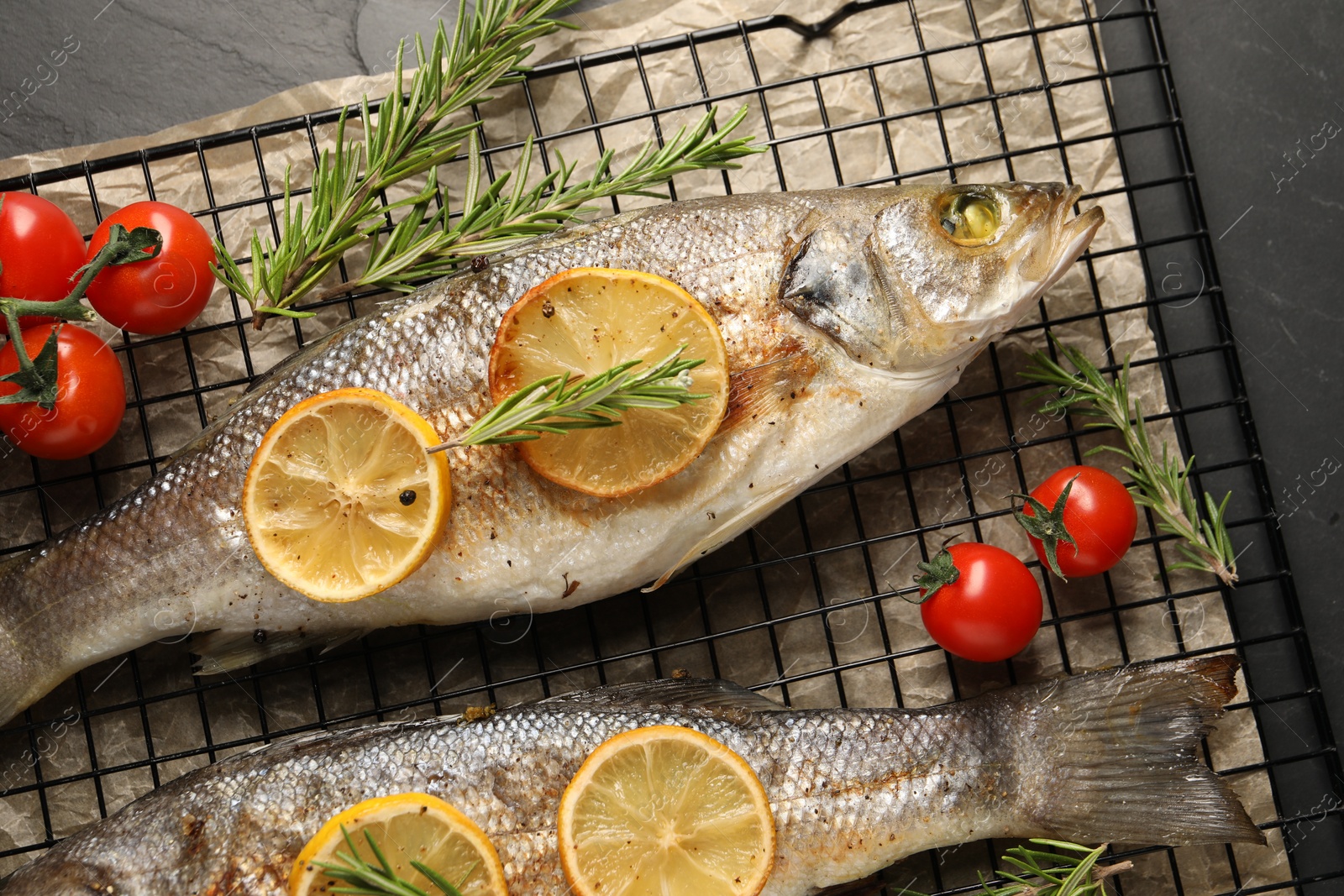 Photo of Baked fish with tomatoes, rosemary and lemon on black textured table, top view