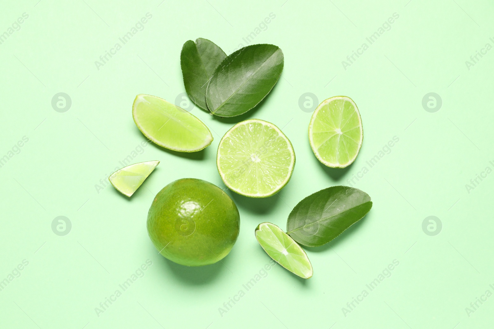 Photo of Whole and cut fresh ripe limes with leaves on light green background, flat lay