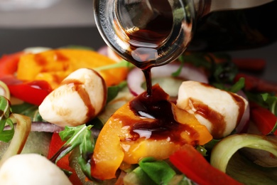 Photo of Pouring balsamic vinegar onto vegetable salad, closeup