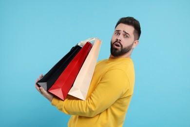 Photo of Shocked man with paper shopping bags on light blue background