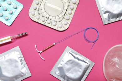 Photo of Contraceptive pills, condoms, intrauterine device and thermometer on pink background, flat lay. Different birth control methods