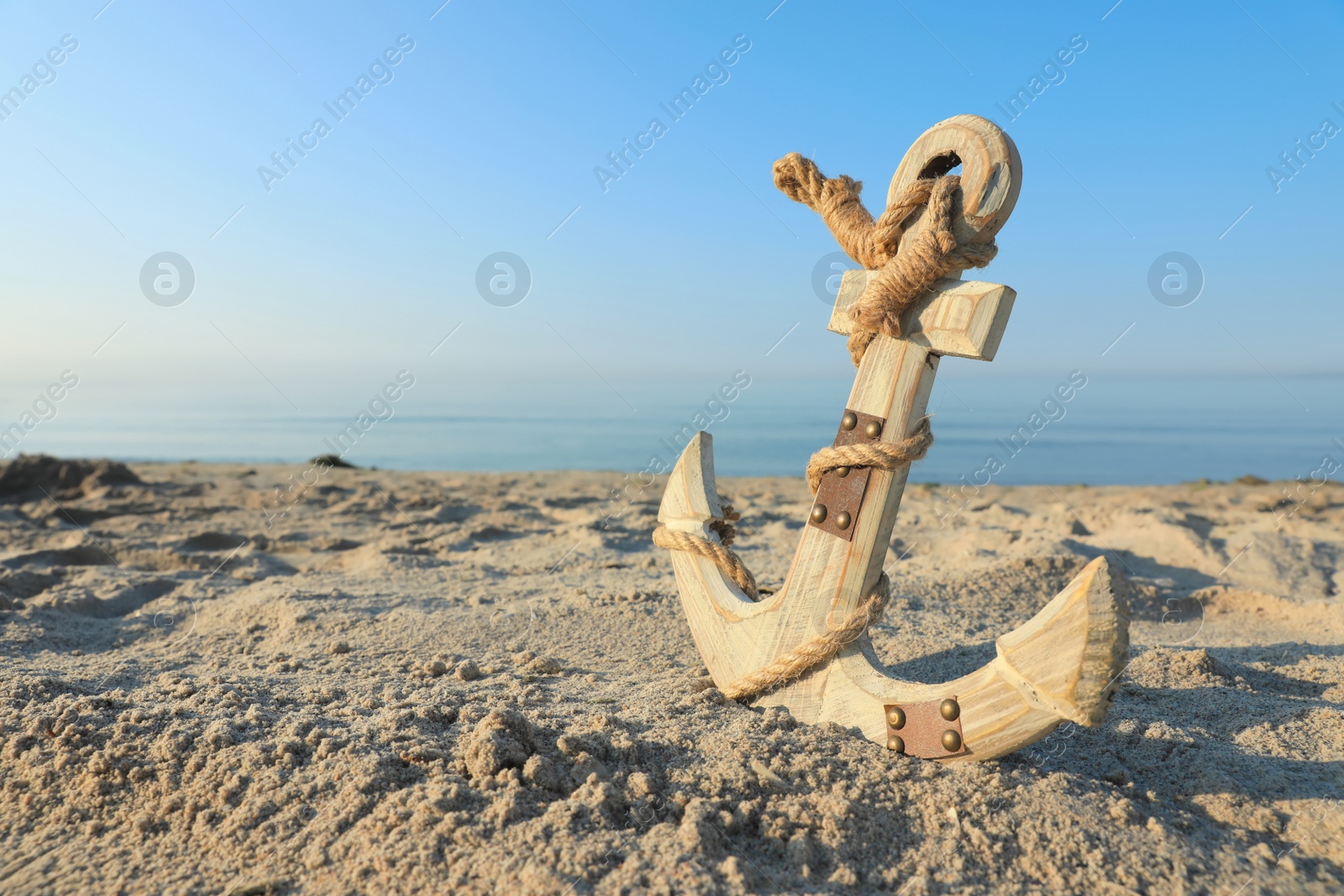 Photo of Wooden anchor with rope on sand near sea. Space for text