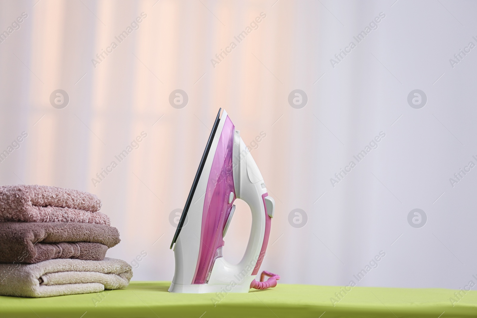 Photo of Modern iron and towels on board against blurred background. Space for text