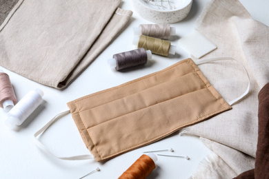 Photo of Homemade protective mask and sewing accessories on white background