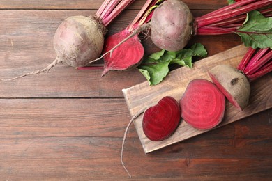 Photo of Cut and whole raw beets on wooden table, flat lay