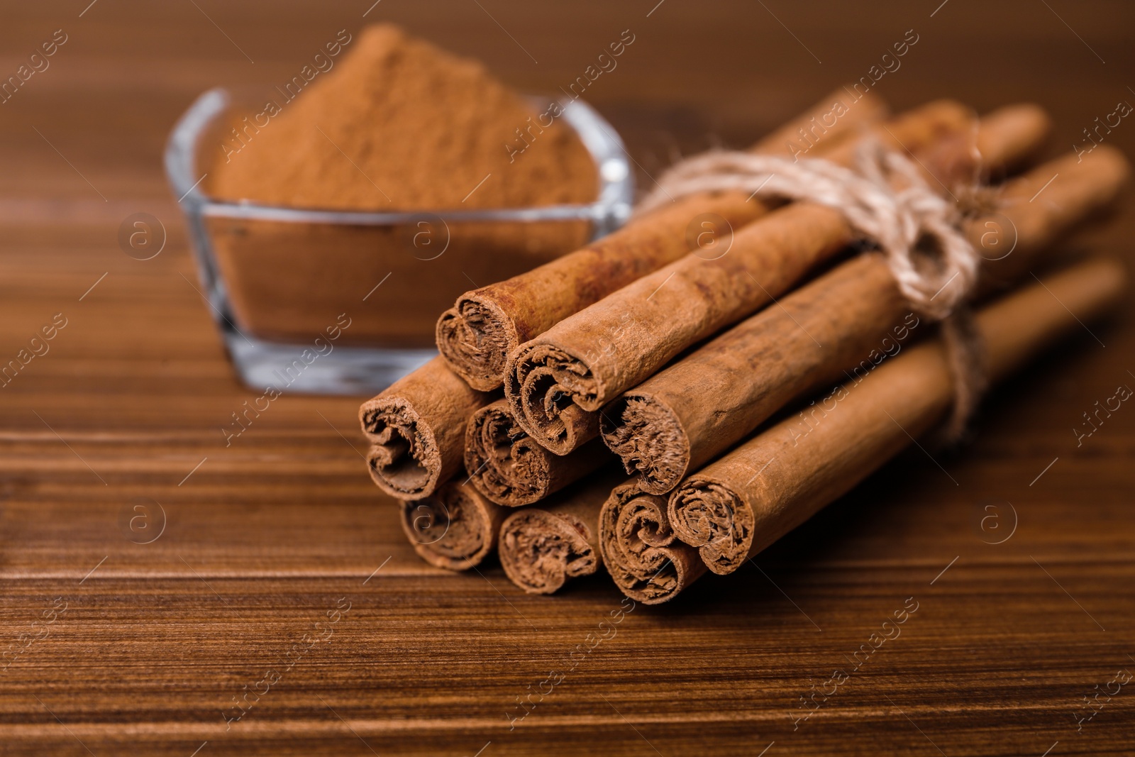 Photo of Aromatic cinnamon sticks and glass bowl with powder on wooden table, closeup