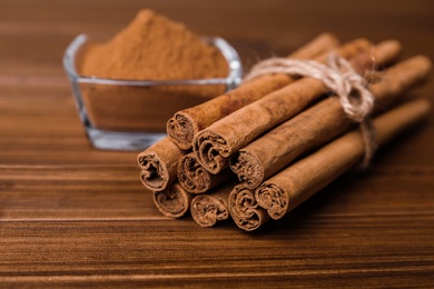 Photo of Aromatic cinnamon sticks and glass bowl with powder on wooden table, closeup