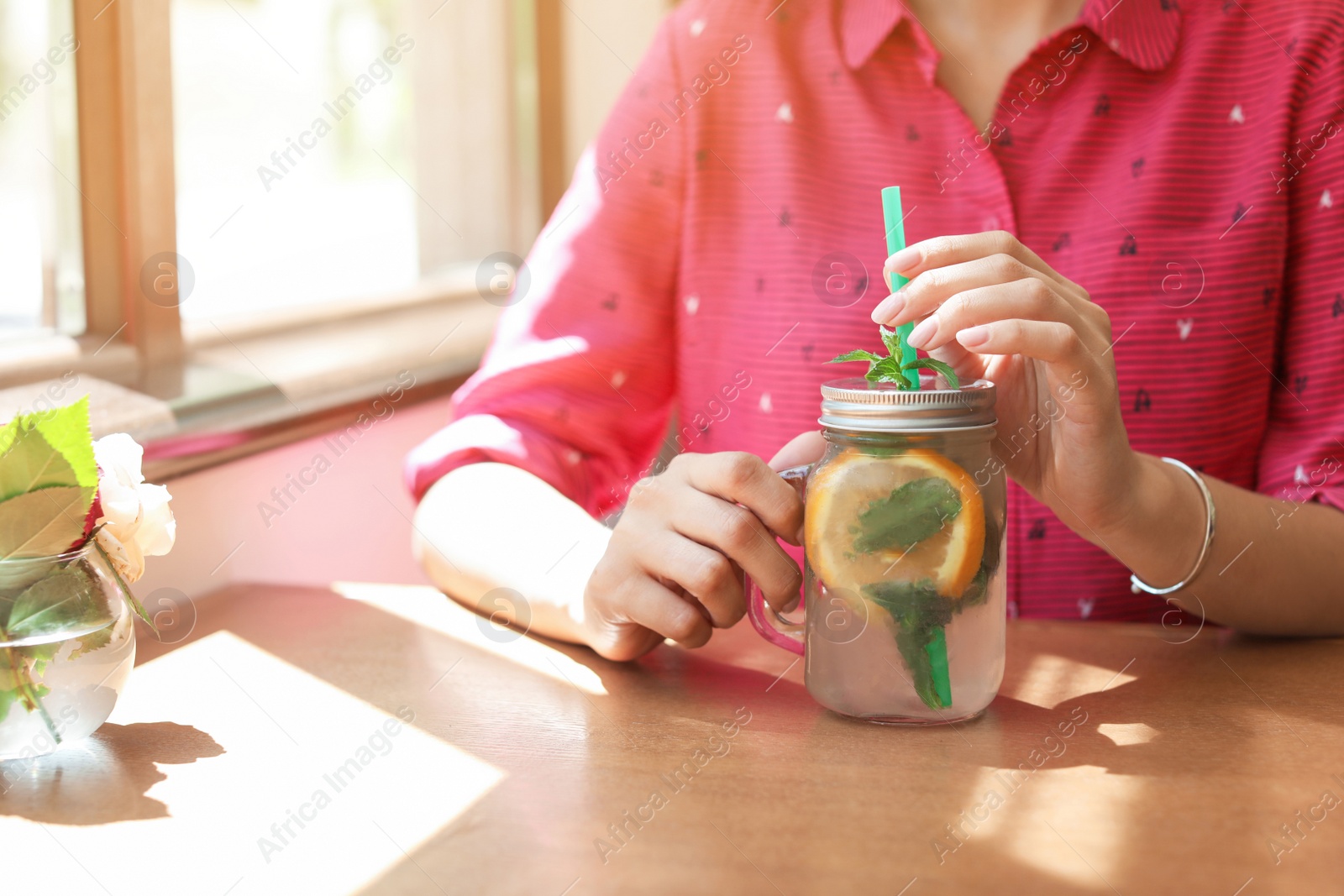 Photo of Young woman with mason jar of tasty natural lemonade in cafe, closeup. Detox drink