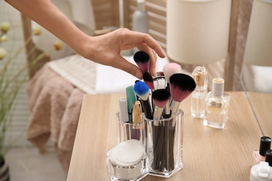 Woman taking brush from organizer for makeup cosmetic products on table