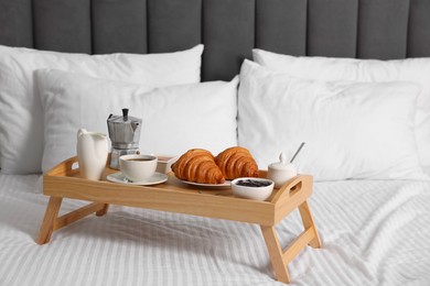Photo of Wooden tray with tasty breakfast on bed at home