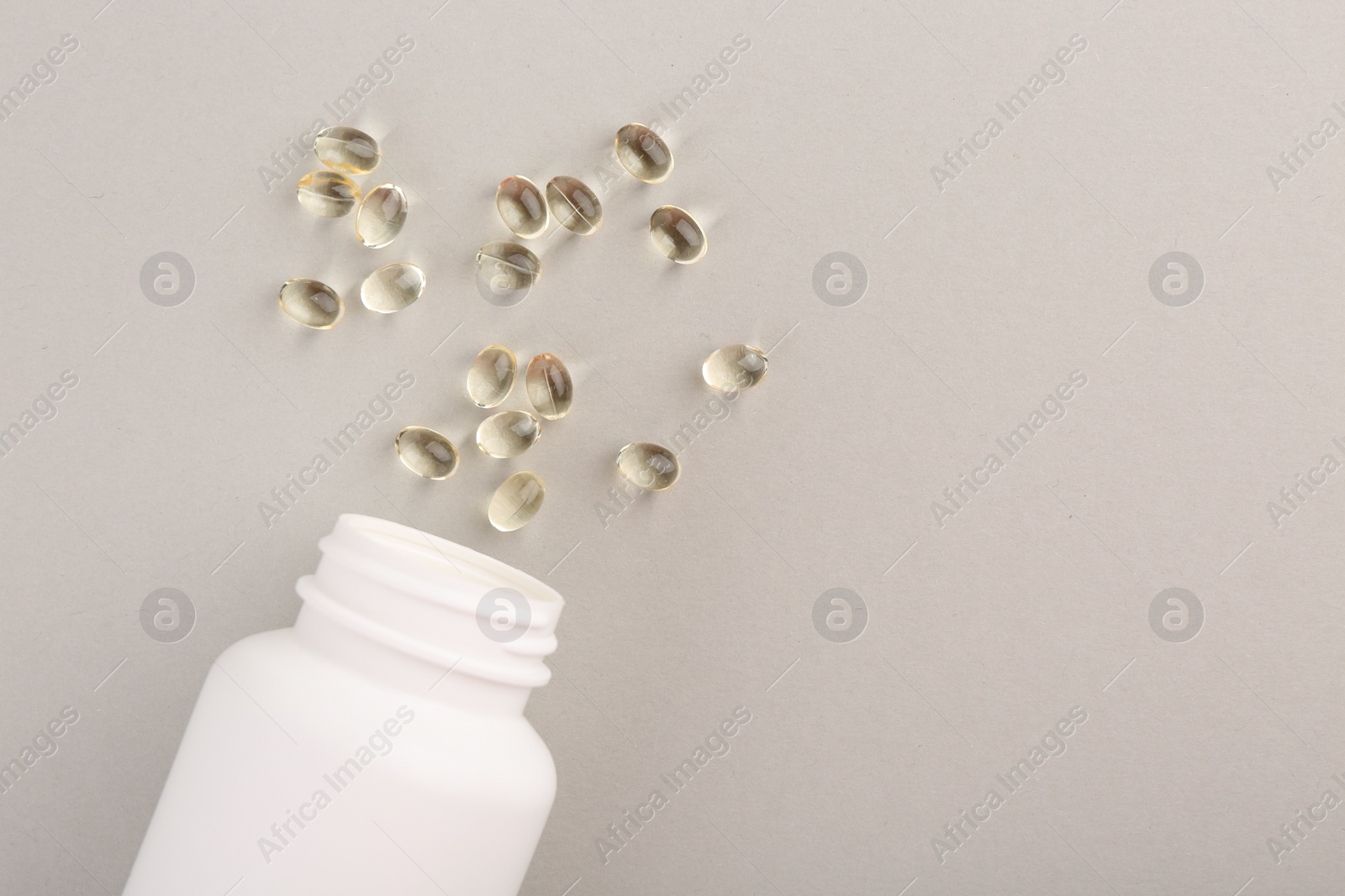 Photo of Bottle and vitamin capsules on light grey background, top view. Space for text