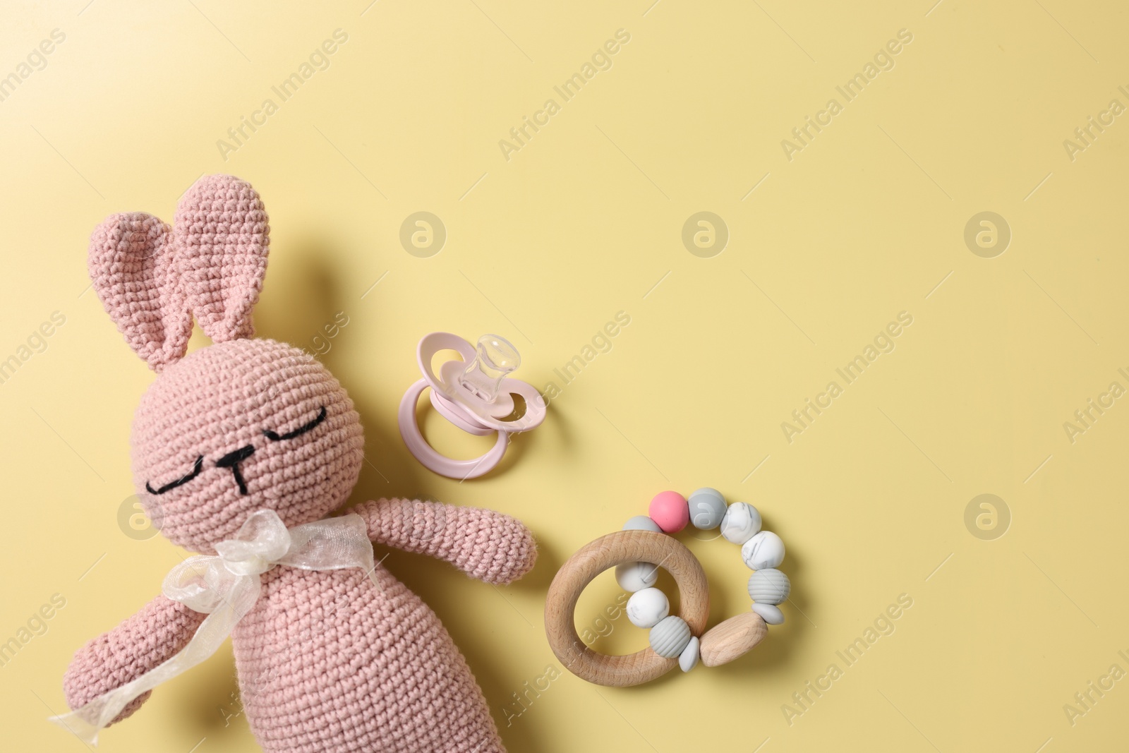 Photo of Baby accessories. Toy rabbit, pacifier and rattle on yellow background, flat lay. Space for text