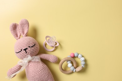 Baby accessories. Toy rabbit, pacifier and rattle on yellow background, flat lay. Space for text