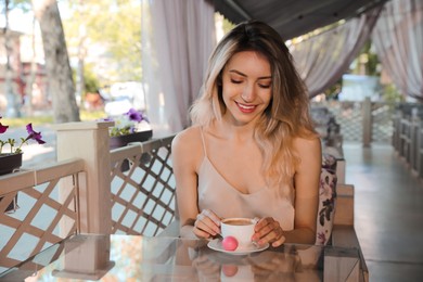 Happy young woman with cup of coffee enjoying early morning on cafe terrace