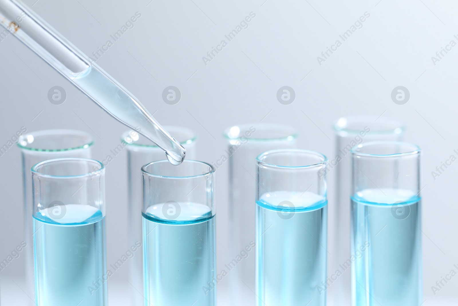 Photo of Dripping liquid from pipette into test tube on light background, closeup