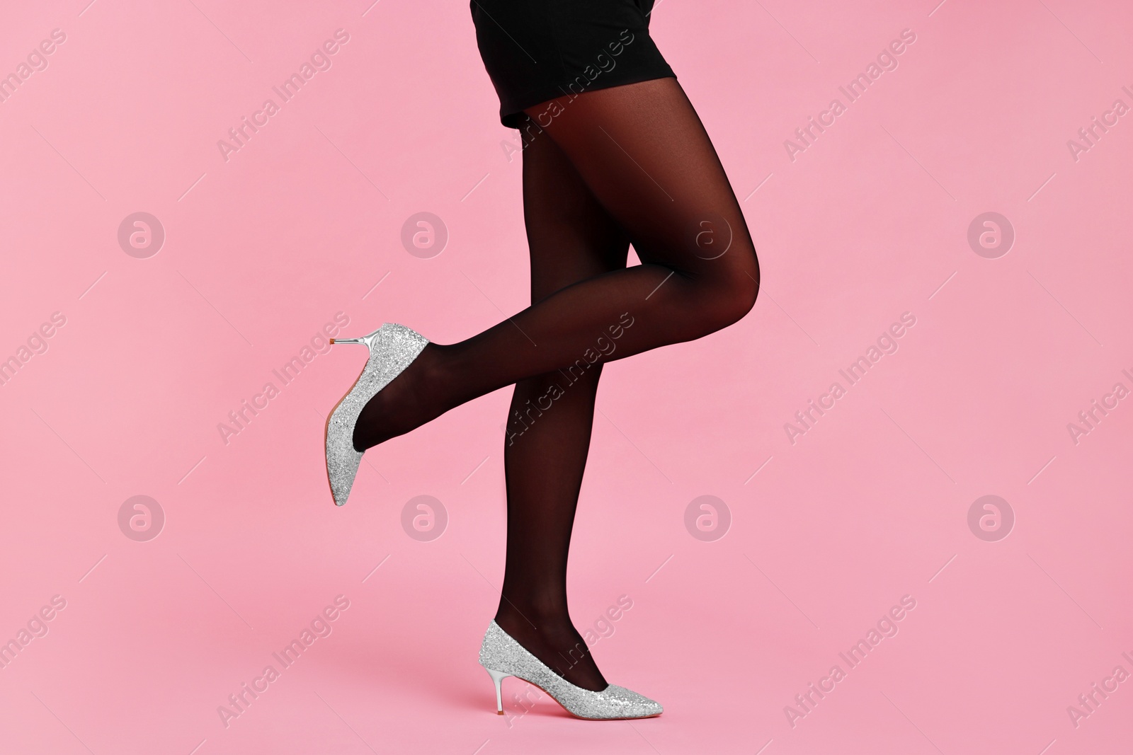 Photo of Woman with beautiful long legs wearing black tights and stylish shoes on pink background, closeup