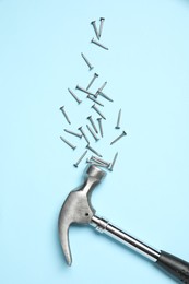 Hammer and metal nails on light blue background, flat lay