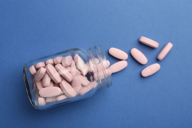 Bottle of pink vitamin capsules on blue background, top view