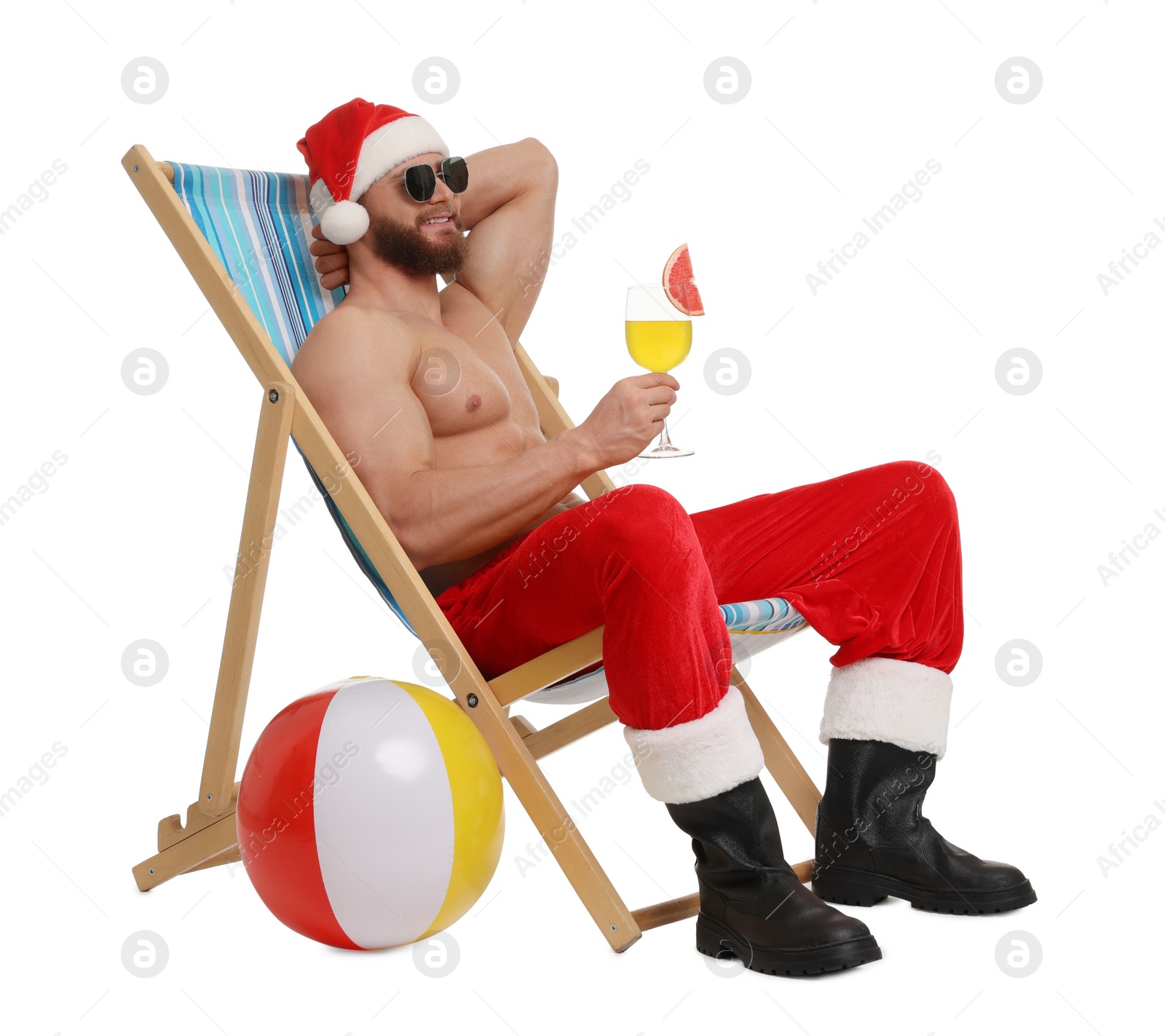 Photo of Muscular young man in Santa hat with deck chair, ball, sunglasses and cocktail on white background