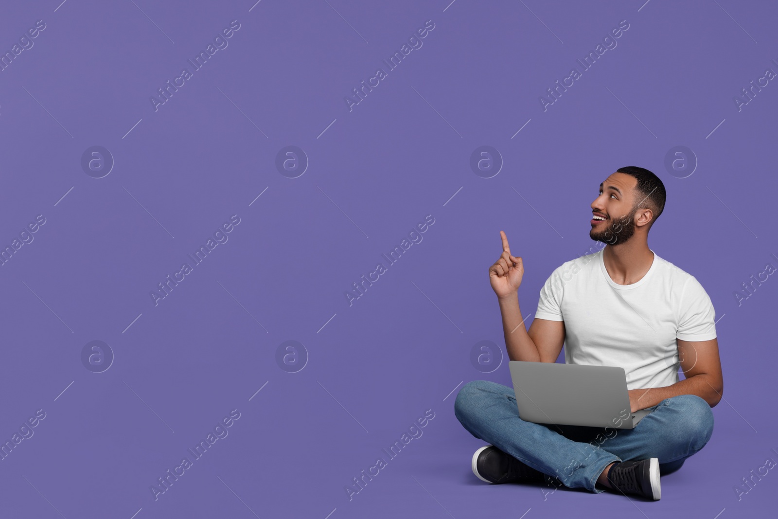 Photo of Smiling young man with laptop on lilac background