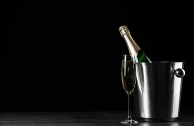 Glass of champagne near bucket with bottle on black background, space for text