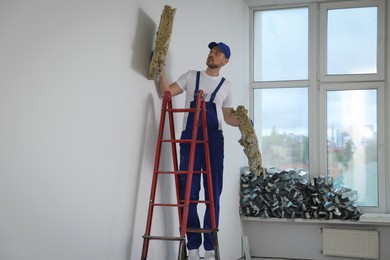 Photo of Construction worker with used glass wool on stepladder in room prepared for renovation