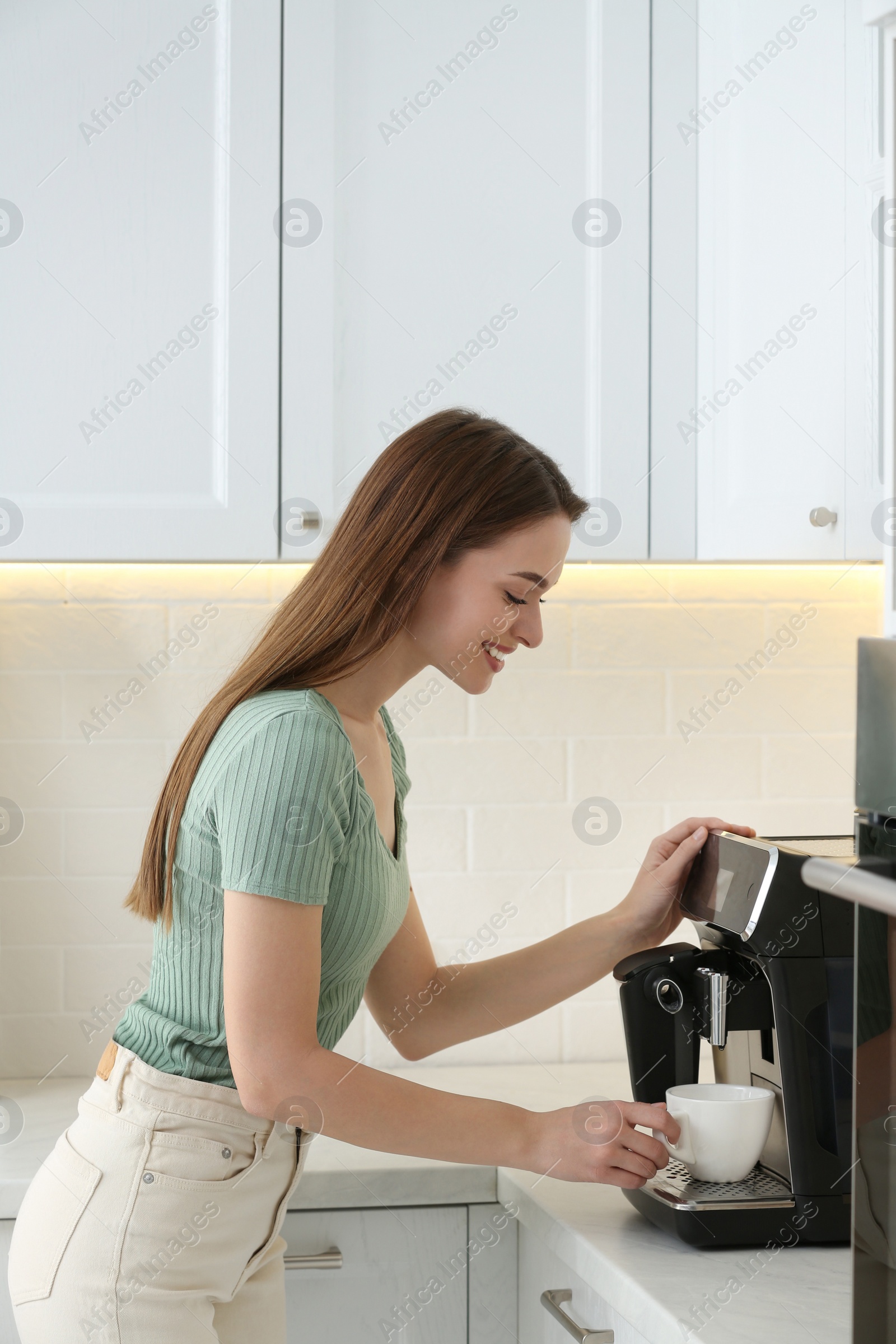 Photo of Young woman preparing fresh aromatic coffee with modern machine in kitchen