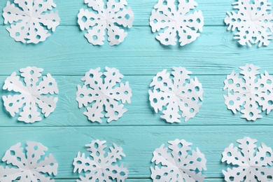 Photo of Many paper snowflakes on turquoise wooden background, flat lay