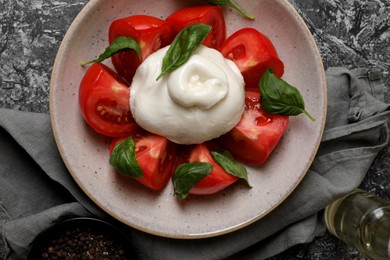 Delicious burrata cheese with tomatoes and basil, oil and peppercorns on grey table, flat lay