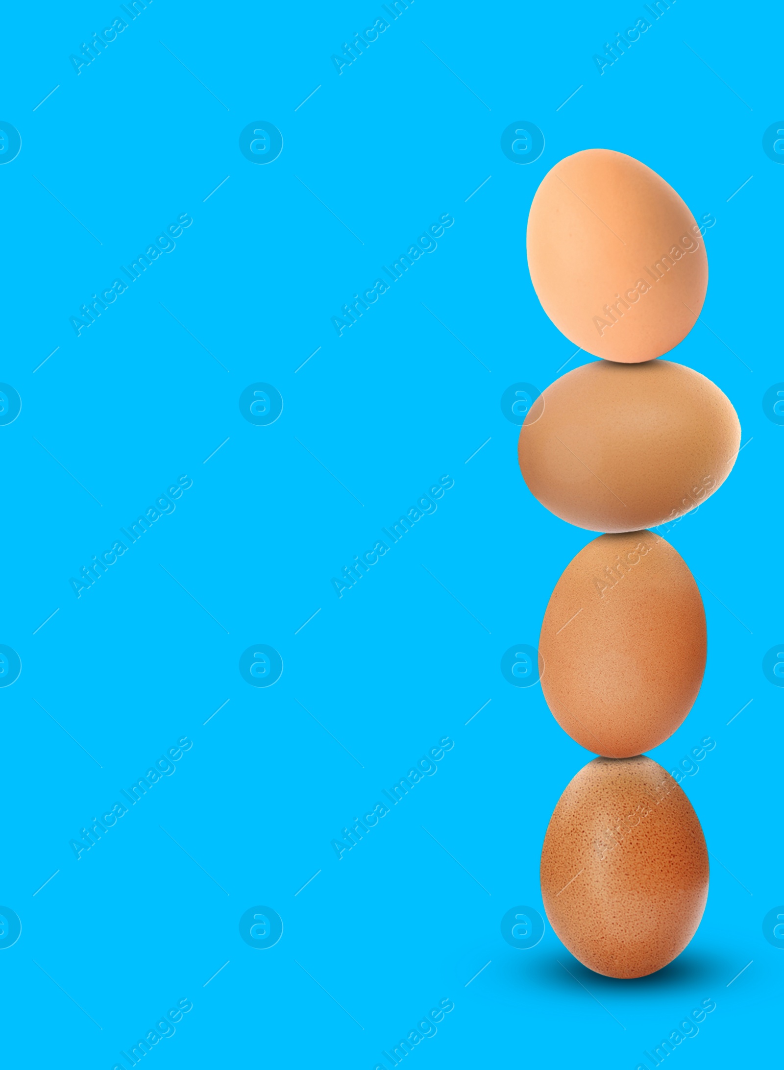 Image of Stacked fresh chicken eggs against light blue background. Space for text