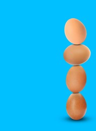 Image of Stacked fresh chicken eggs against light blue background. Space for text