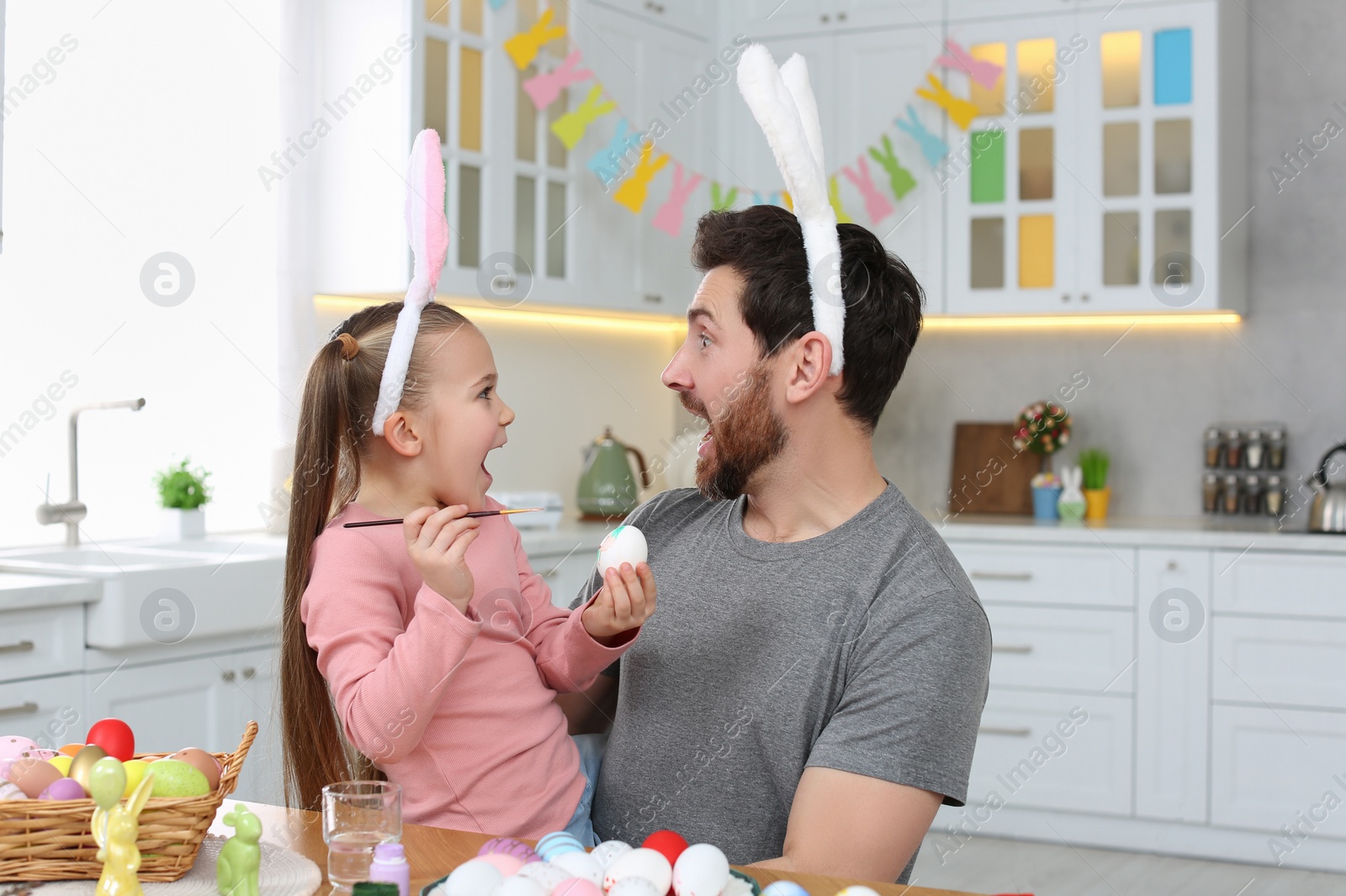 Photo of Emotional father with his cute daughter and Easter eggs at table in kitchen