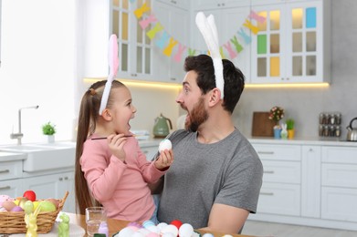 Emotional father with his cute daughter and Easter eggs at table in kitchen