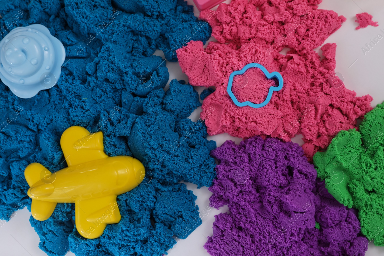 Photo of Bright kinetic sand and toys on white table, flat lay