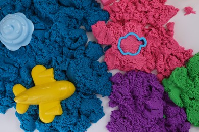 Bright kinetic sand and toys on white table, flat lay