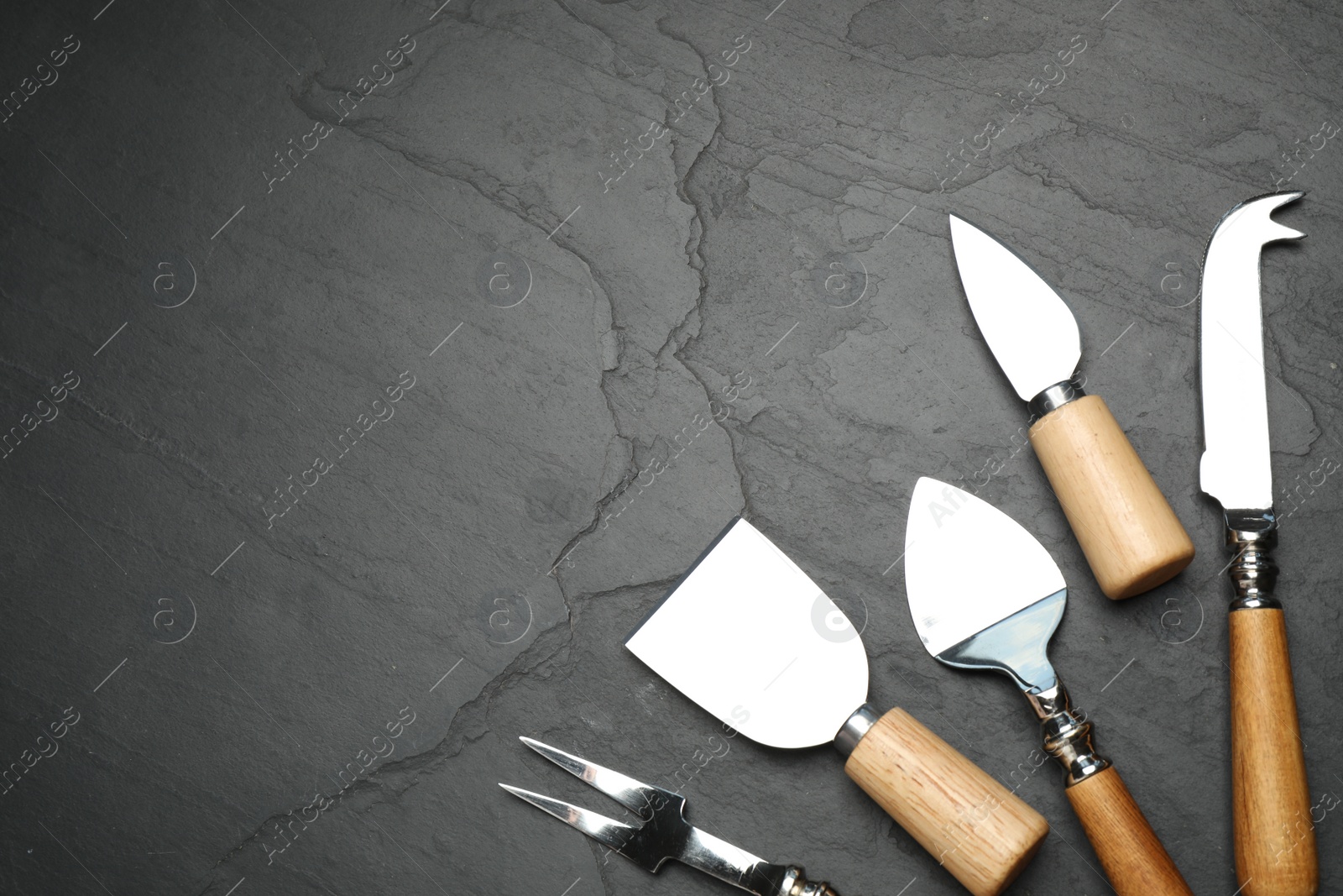 Photo of Cheese knives and fork on black stone table, flat lay. Space for text