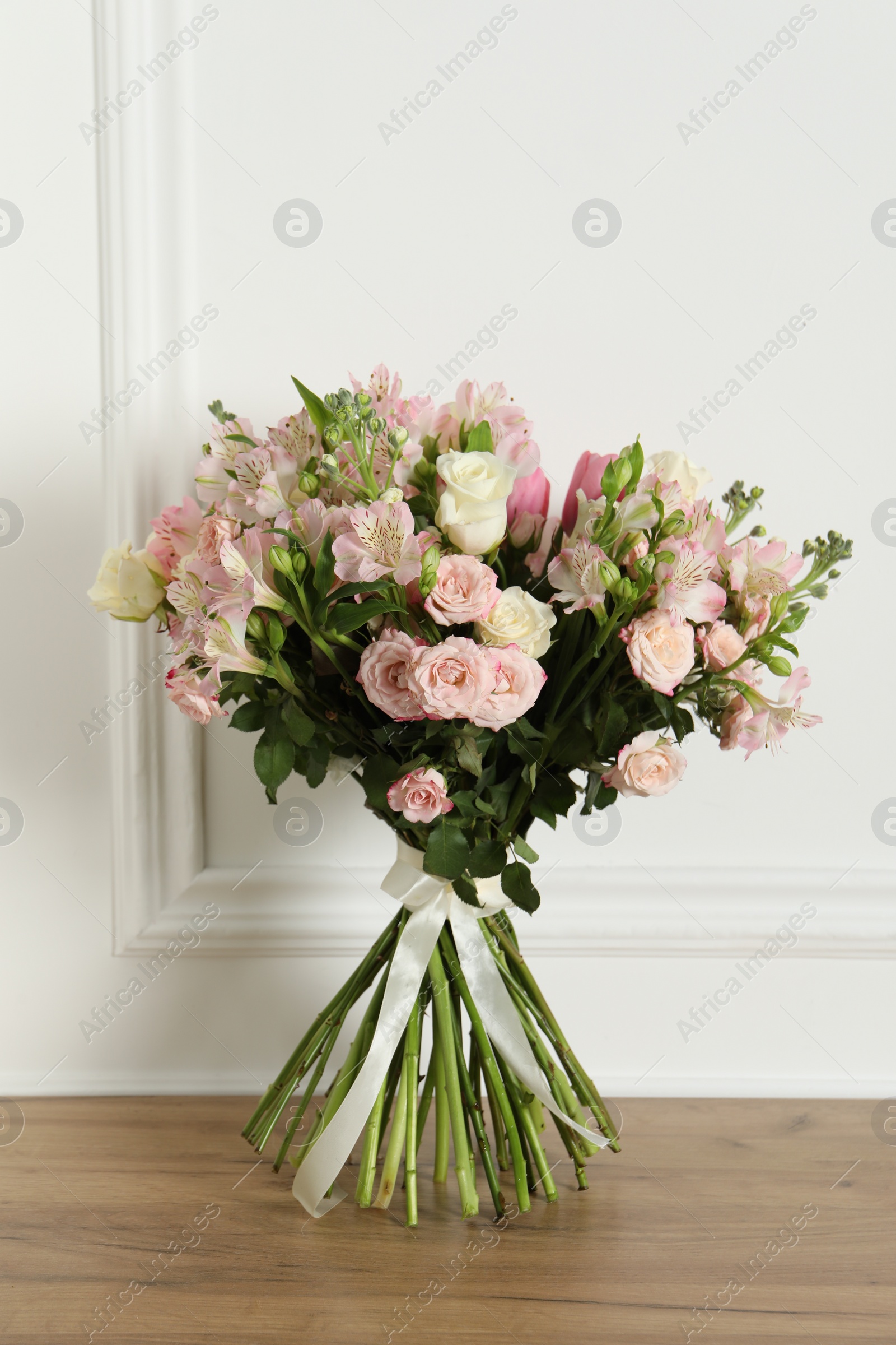 Photo of Beautiful bouquet of fresh flowers on wooden table near white wall